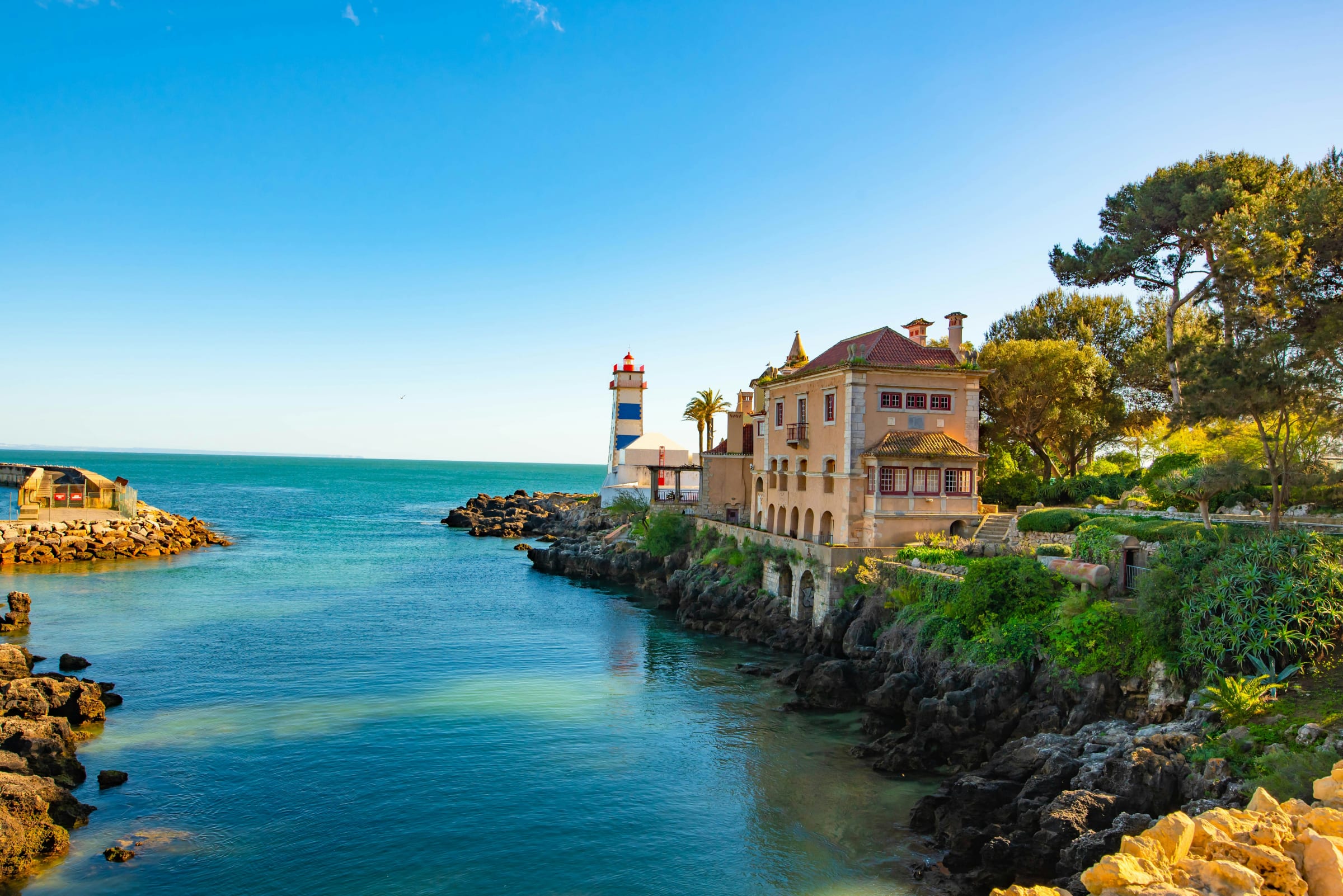 Un phare et une villa au bord de l'eau sous un ciel bleu.