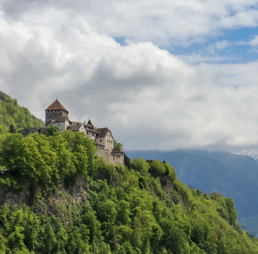 white and brown concrete building on top of green mountain under white clouds during daytime