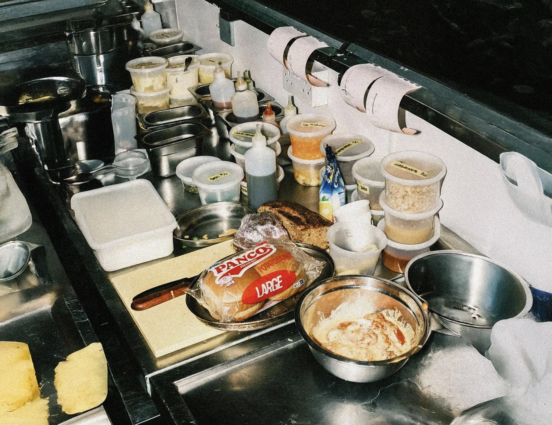 Comptoir de cuisine de food truck encombré avec des ingrédients, des sauces et un sac de pains Panco®, illustrant l'activité intense et les défis des volumes irréguliers.