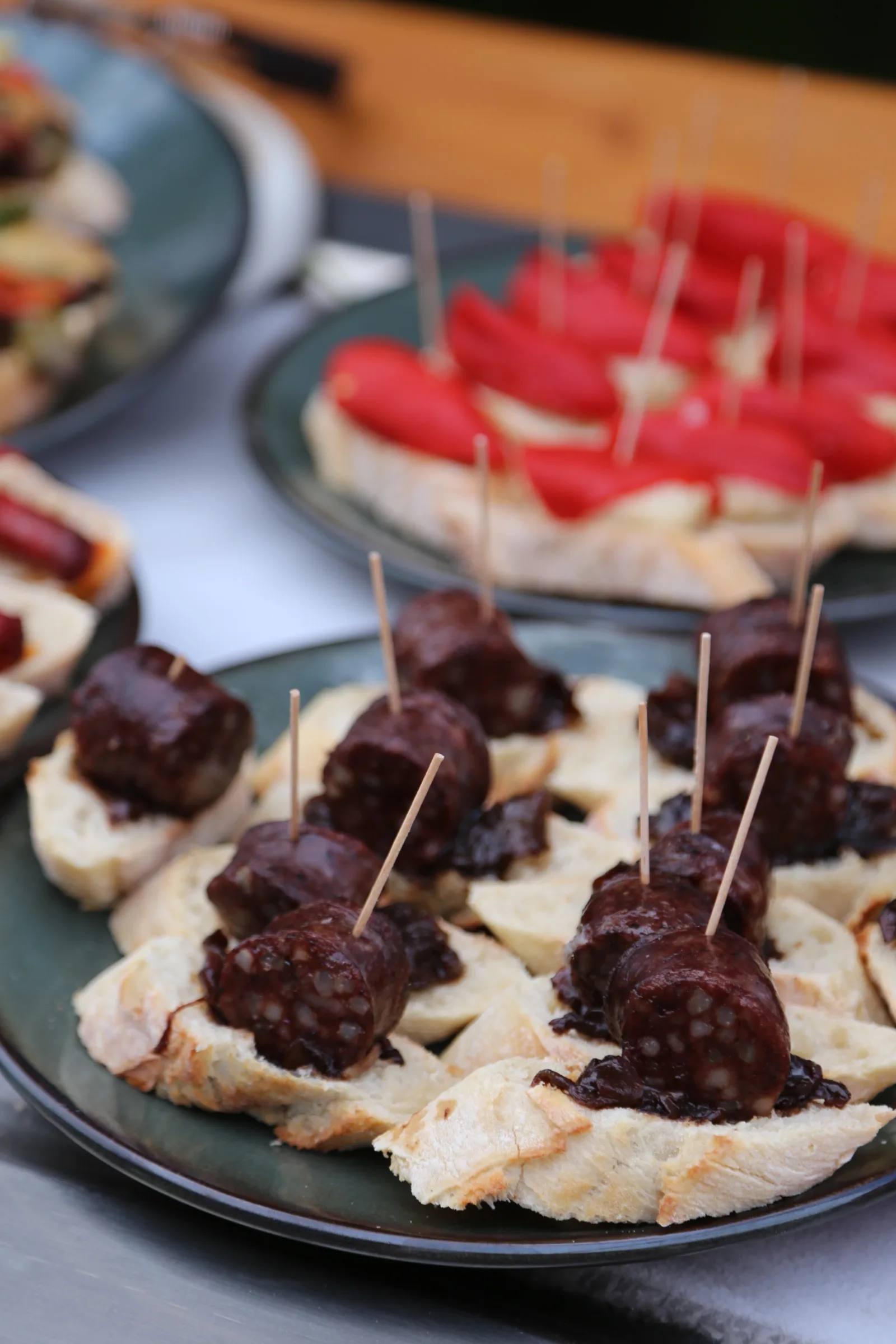 Plates of tapas featuring sliced sausage on bread with toothpicks.