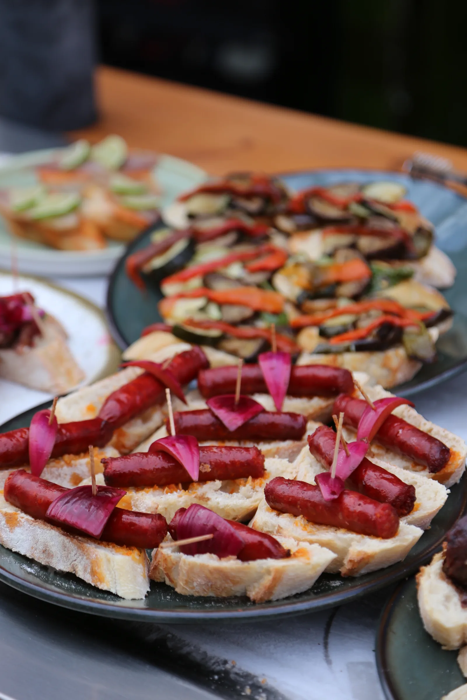 Platter of gourmet hot dogs with pickled onions and assorted appetizers.