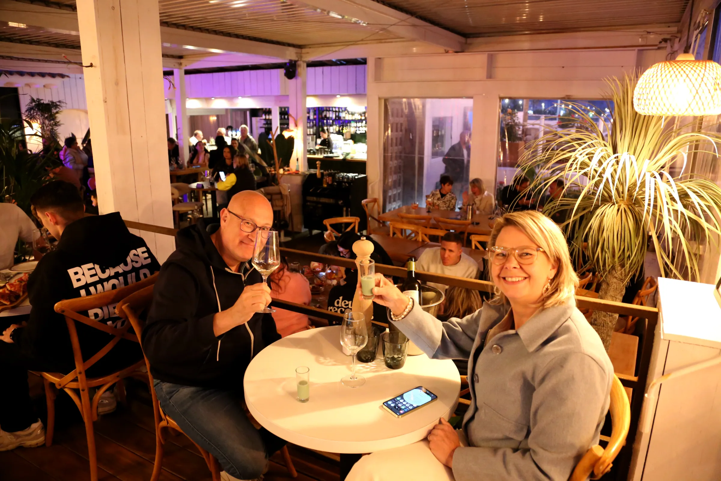 Two people toasting with drinks at a restaurant table.