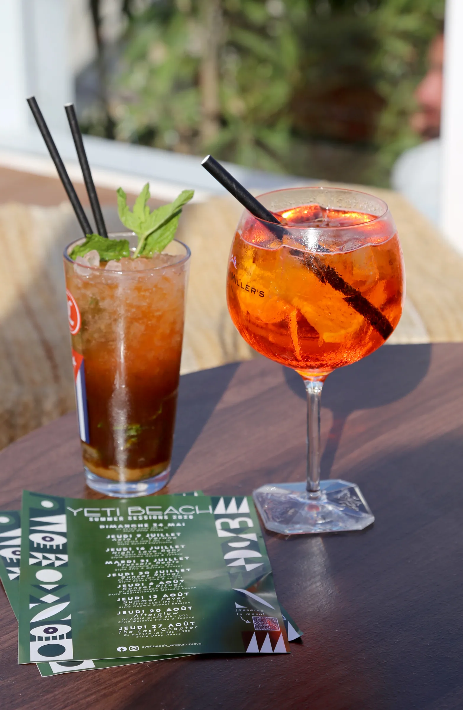Two cocktails on a wooden table with a menu in the foreground.
