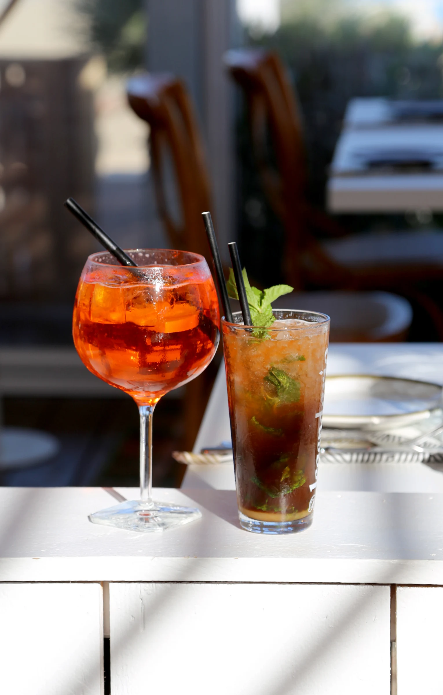 Two cocktails on a table, one in a large glass and one in a tall glass.