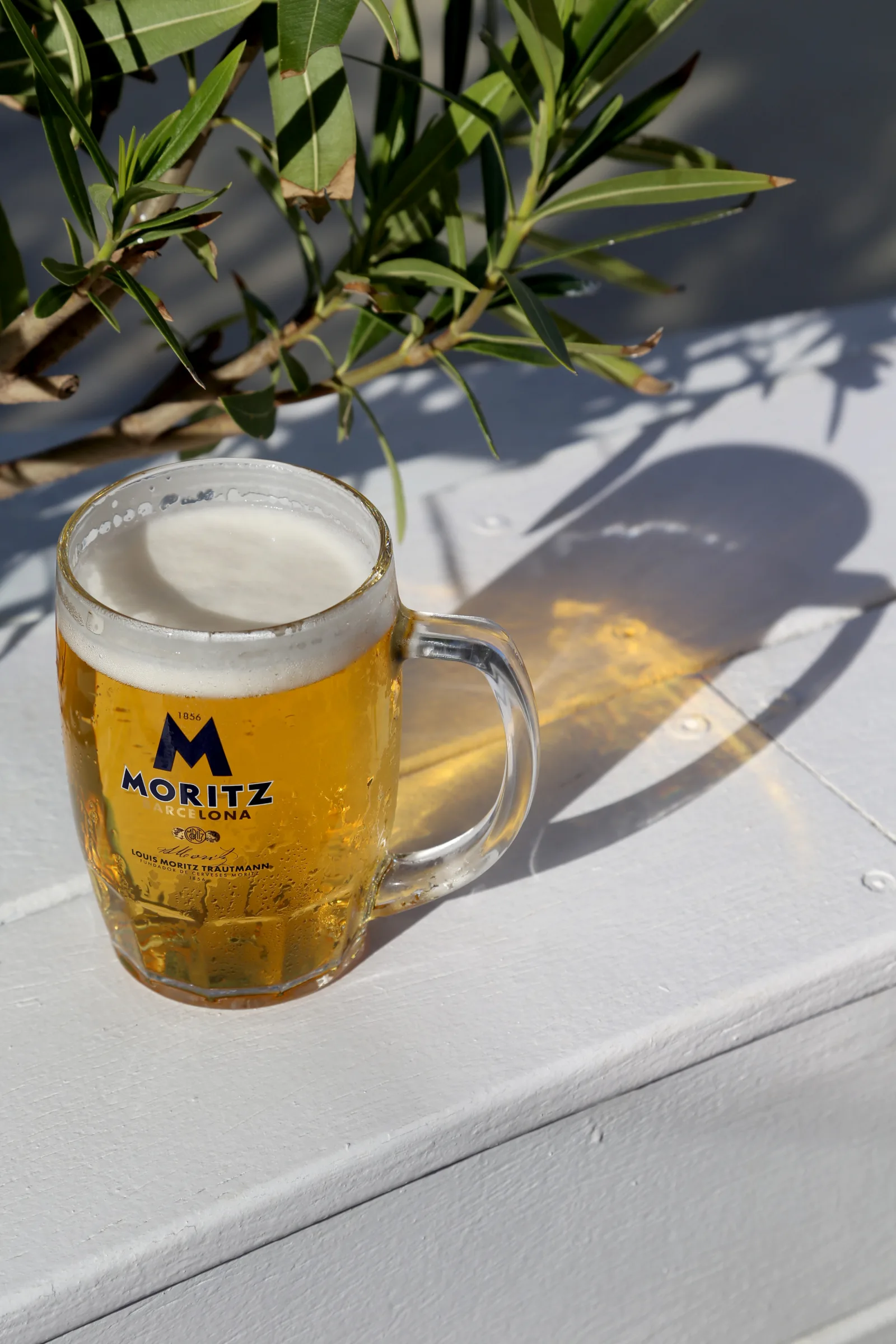 A glass of Moritz beer on a white surface with a shadow.