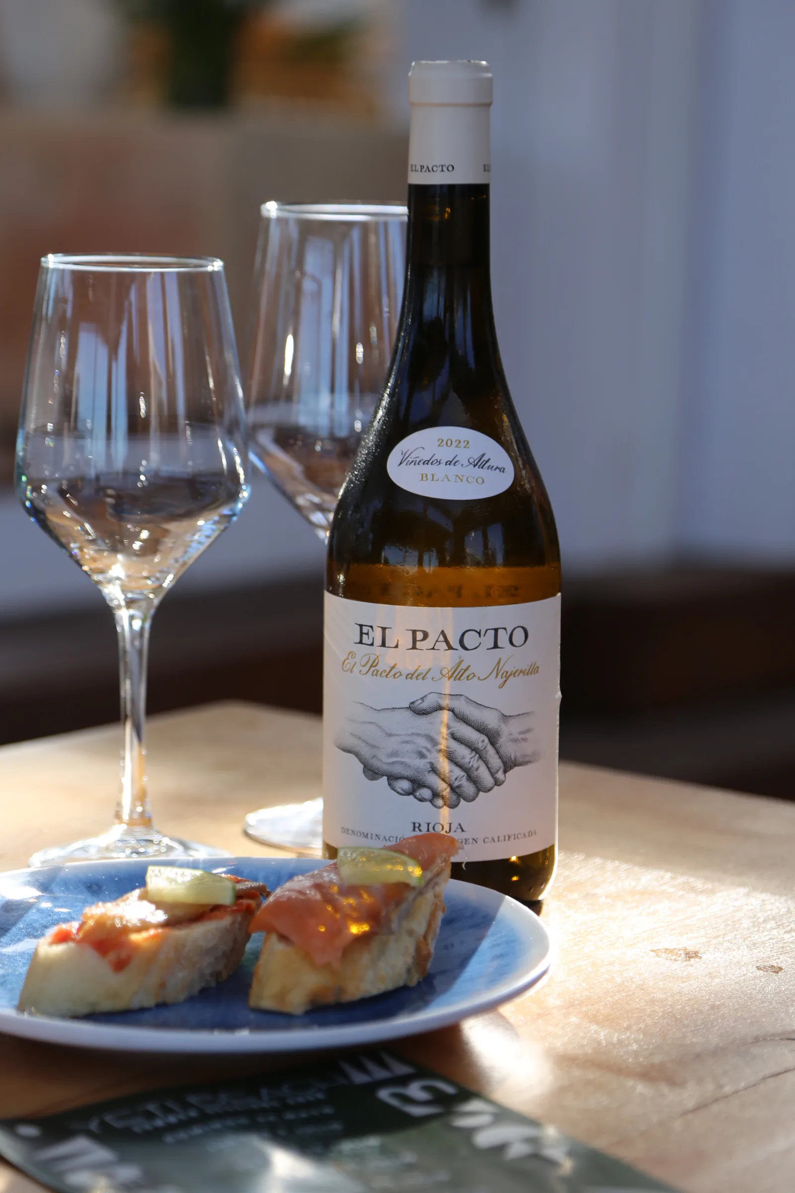 A bottle of El Pacto wine with glasses and a plate of tapas.