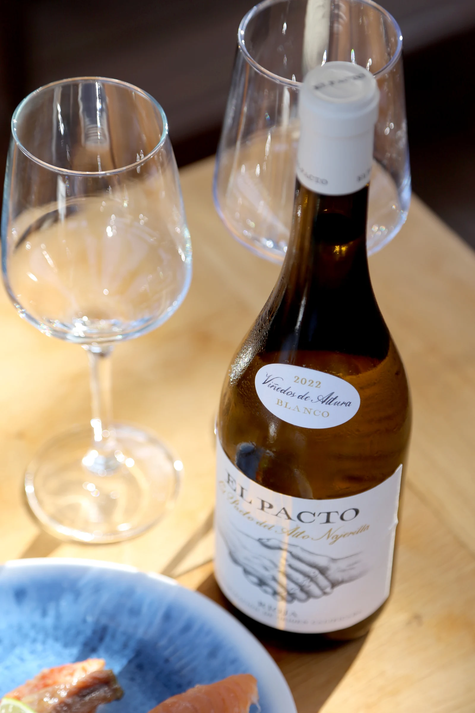 Bottle of El Pacto white wine with glasses on a wooden table.