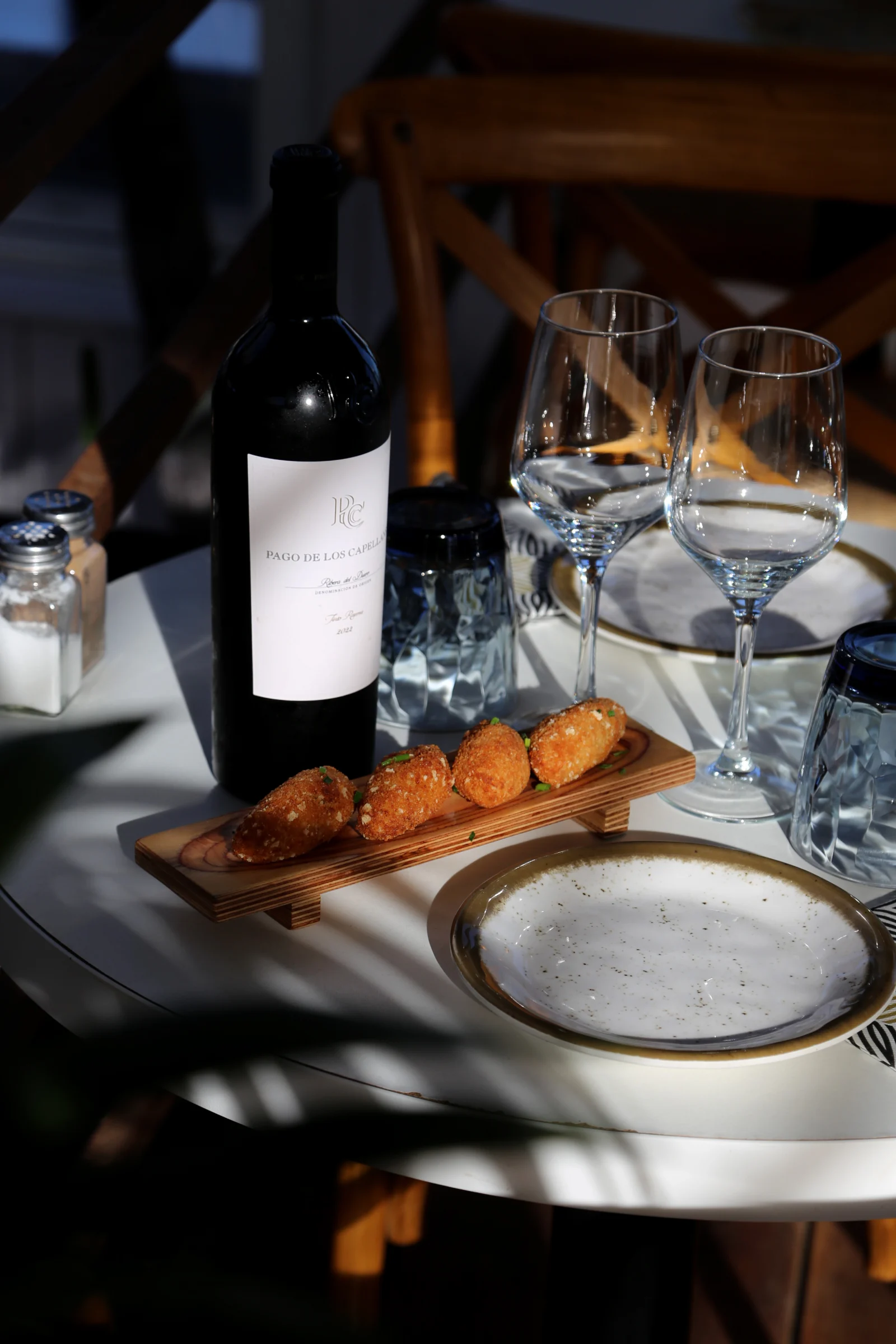 A table setting with a bottle of wine, glasses, and appetizers.