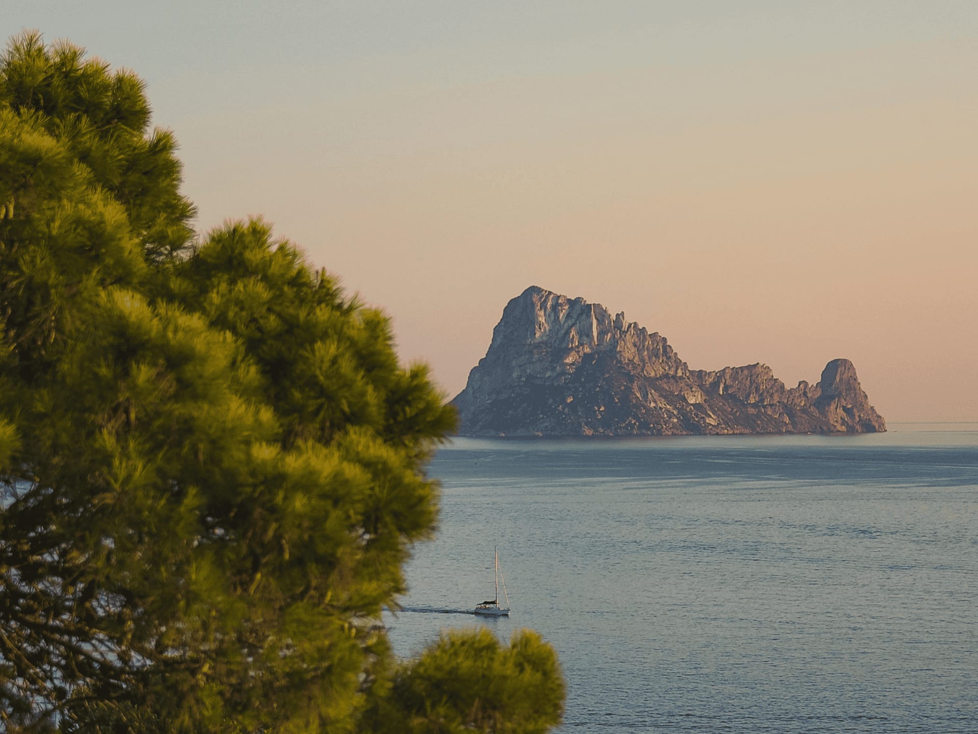 Scenic view of a rocky island at sunset with a sailboat nearby.