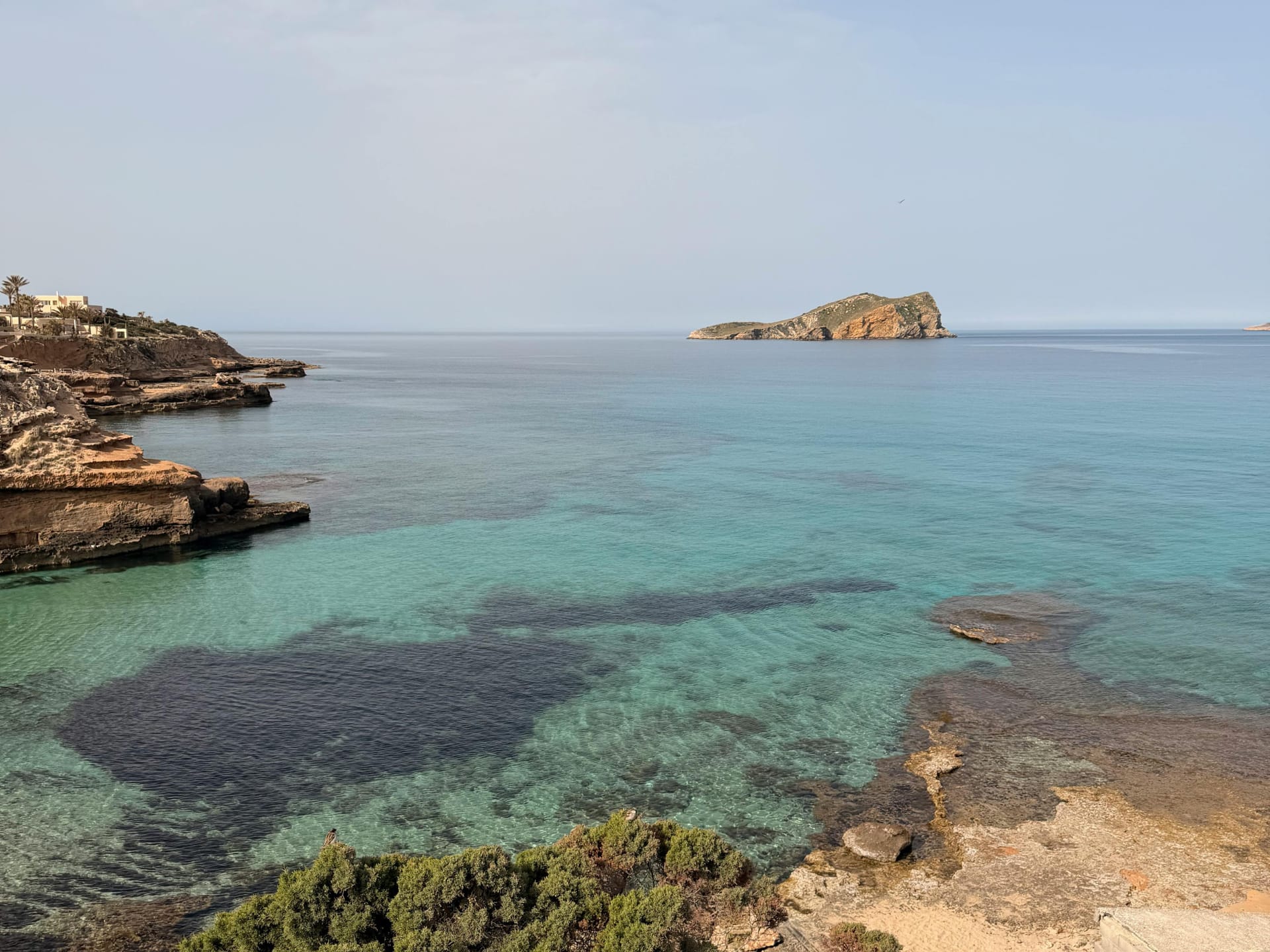 Scenic view of turquoise waters and rocky coastline with an island in the distance.