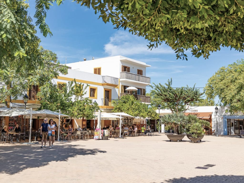 Sunny outdoor plaza with cafes and people in Ibiza.
