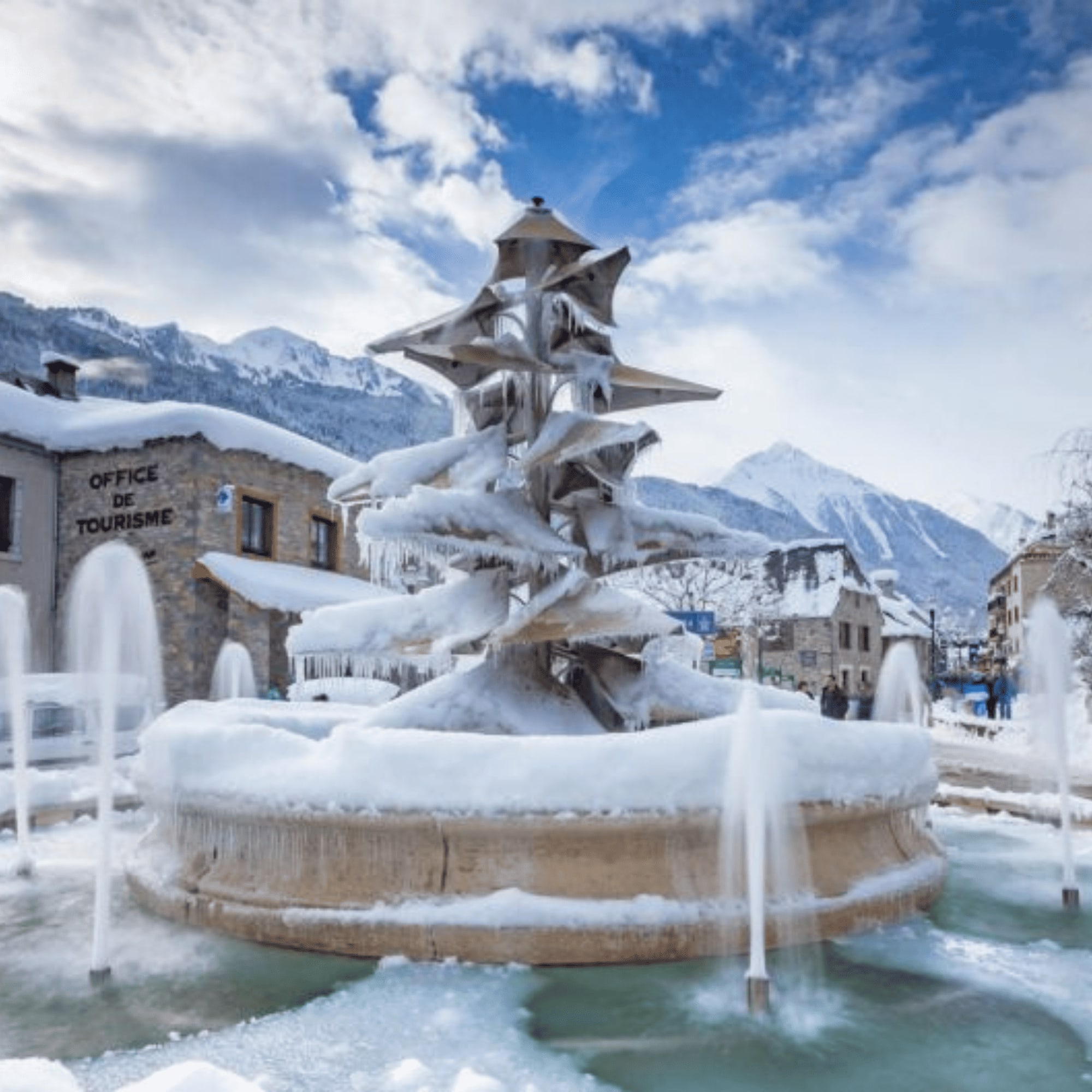 Fontaine gelée entourée de neige avec des montagnes en arrière-plan.