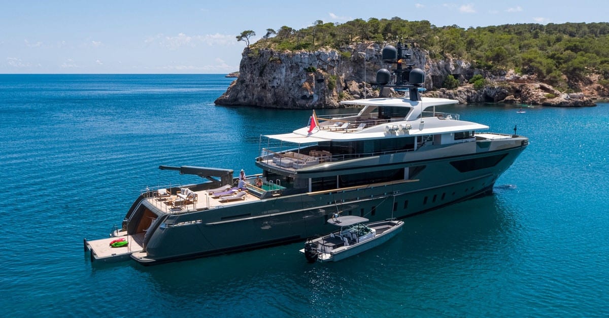 Luxury yacht anchored in turquoise waters with cliffs in the background.